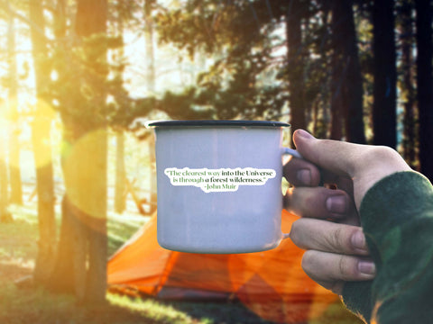 Image shows a hand holding a coffee mug with a Hand holding an John Muir naturalist sticker for the outdoor lovers. The quote reads, "The clearest way into the universe is through a forest wilderness."