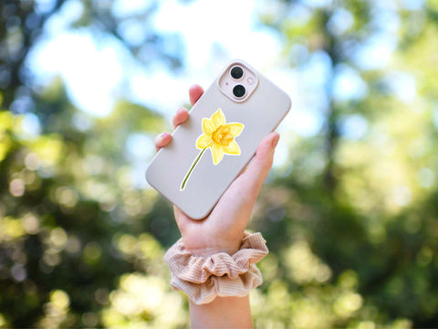 image shows someone holding a cell phone up that has a yellow daffodil sticker on the phone case.