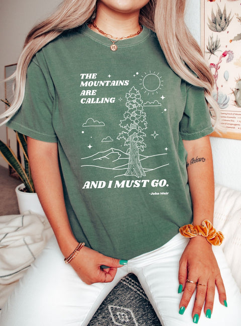 Woman wearing a nature lover T-shirt portrays a Redwood tree, mountains, and the John Muir quote, "the mountains are calling, and I must go."