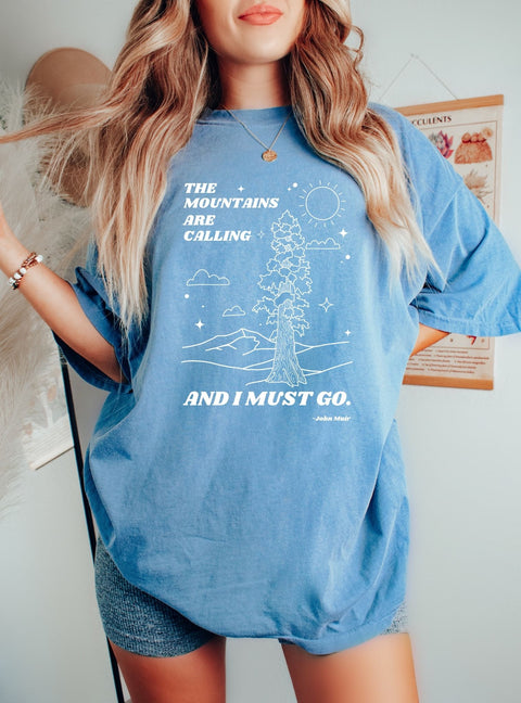Woman wearing a nature lover T-shirt portrays a Redwood tree, mountains, and the John Muir quote, "the mountains are calling, and I must go."