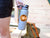 image shows a cave sticker on a gray sport water bottle held by a female hiker.