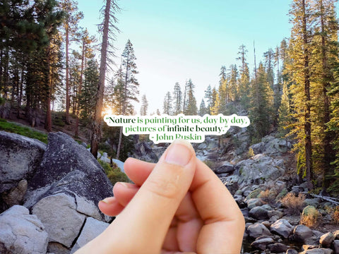  Image shows a hand holding a "Nature is painting for us, day by day, pictures of infinite beauty" John Ruskin literary quote sticker for readers, journalers, and nature lovers!