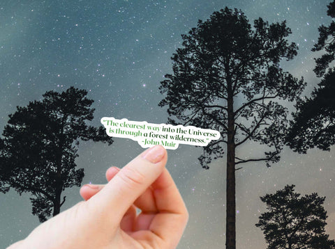 Hand holding an John Muir naturalist sticker for the outdoor lovers. The quote reads, "The clearest way into the universe is through a forest wilderness."