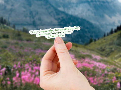Image shows a hand holding a "Nature is painting for us, day by day, pictures of infinite beauty" John Ruskin literary quote sticker for readers, journalers, and nature lovers!