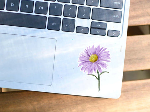 image shows a small purple flower sticker on a laptop.