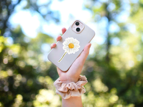 image shows someone holding a cell phone case which has a white daisy sticker on it.
